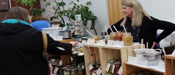Person shopping at table stocked with jams and salesperson behind