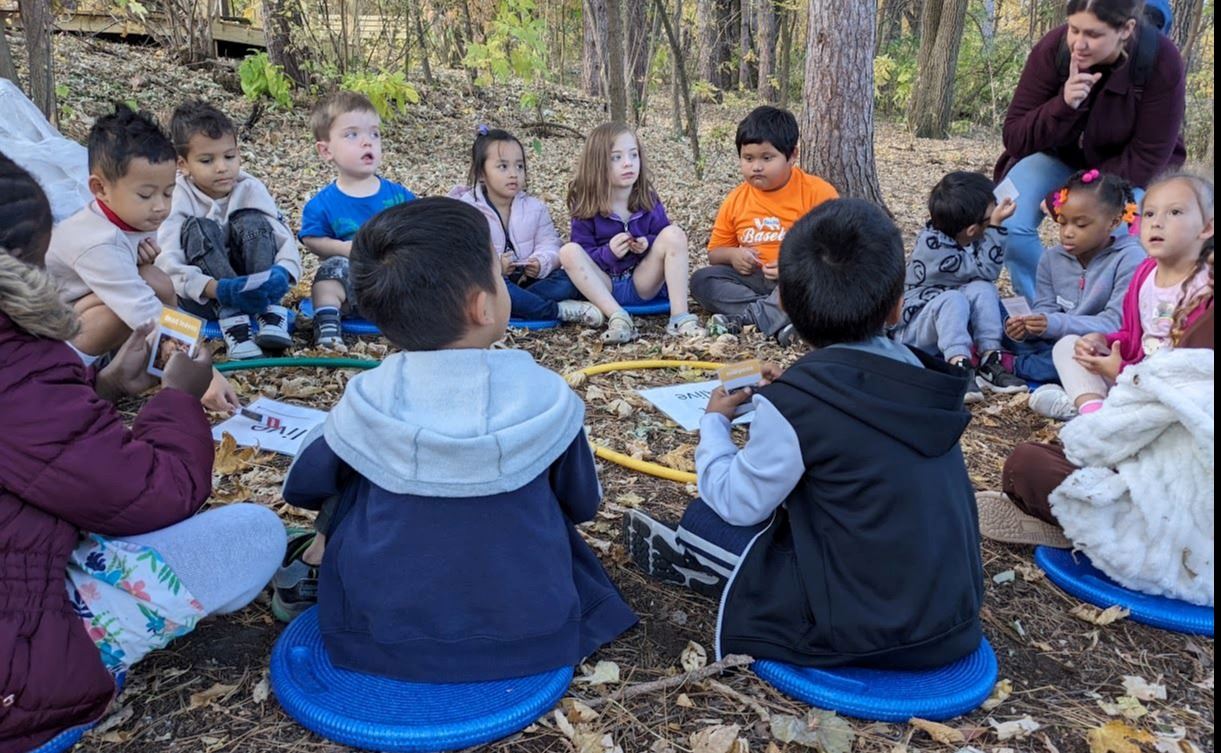 Class of children sits on blue circles in the forest